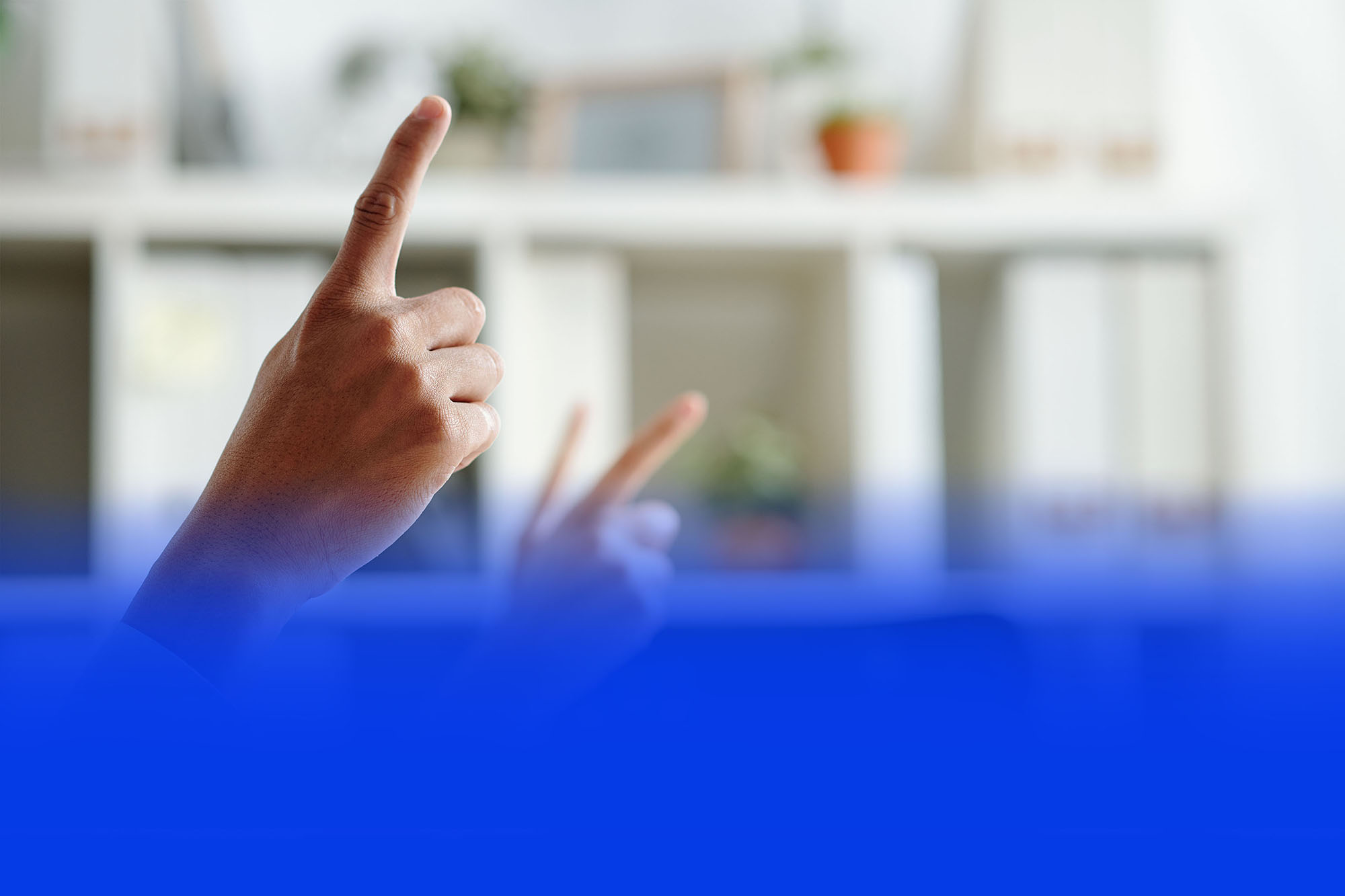 Hand zeigt auf eine Telefonanlagen-Funktion vor unscharfem Bürohintergrund